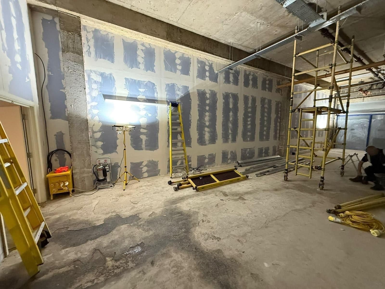 Shop unit during construction with plasterboard walls, a tower scaffold and a worker crouching at the right