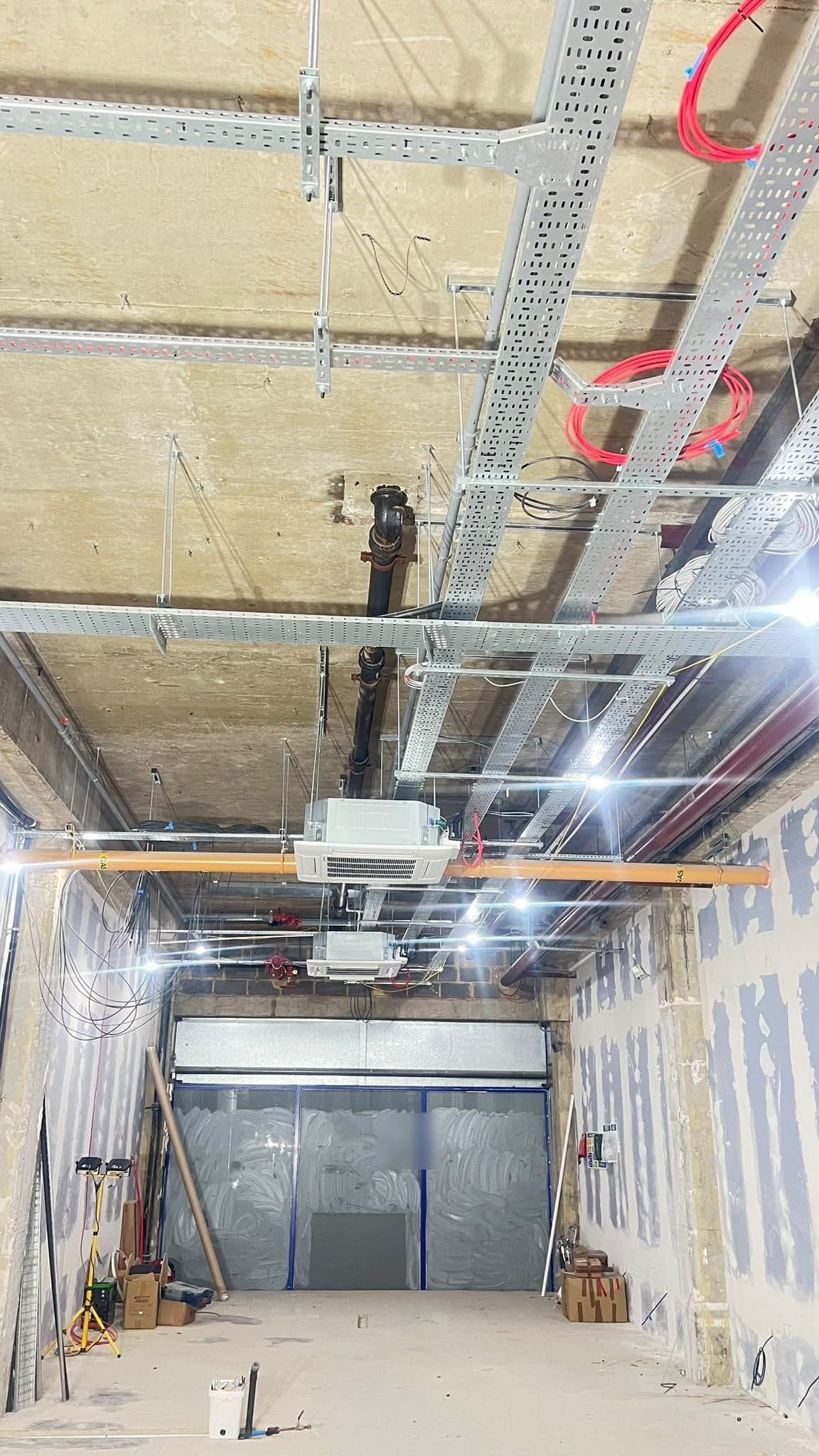 Shop unit ceiling with cable trays, pipework and two air conditioning cassette units, looking towards the shopfront