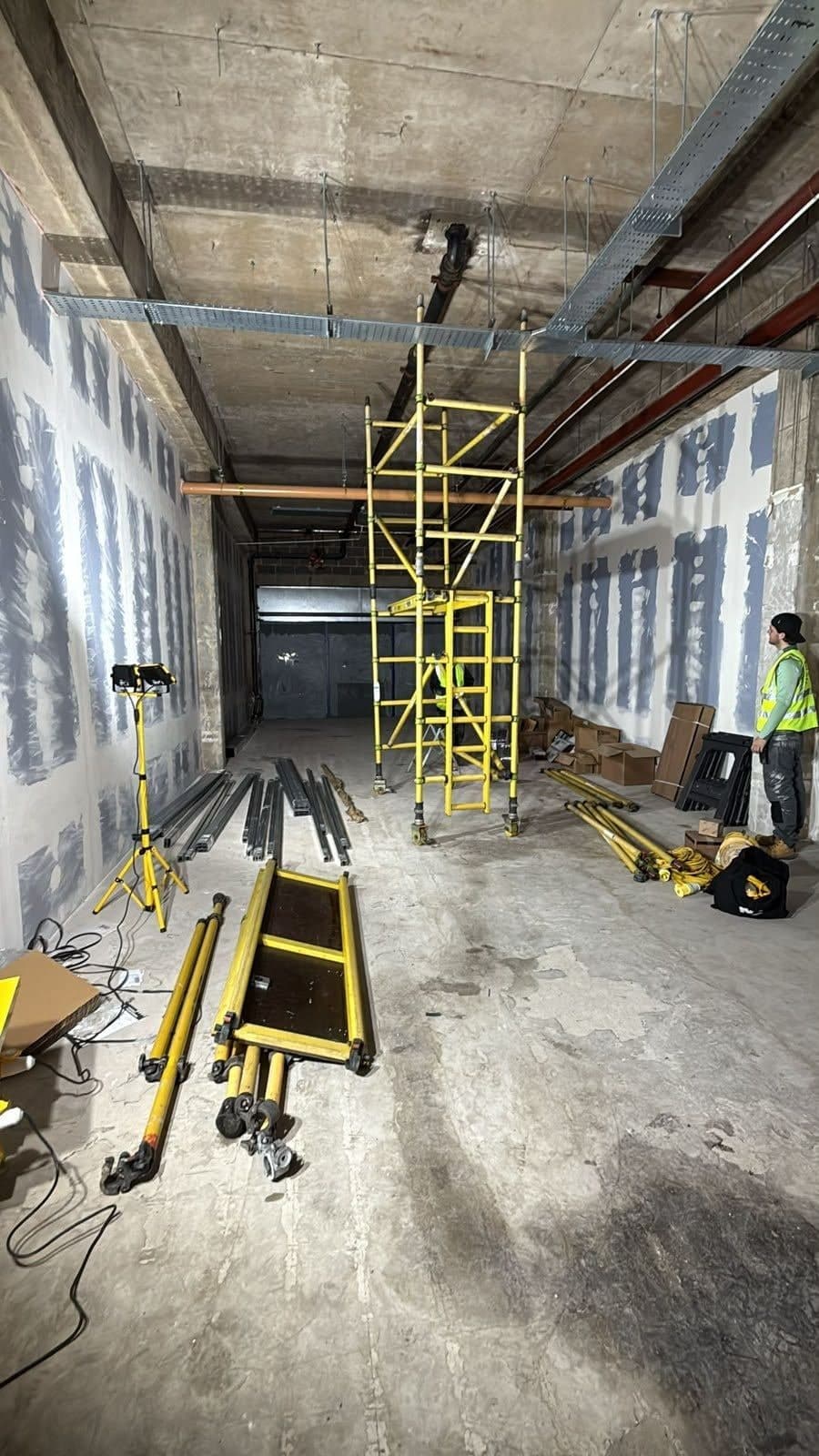 Long shop unit during construction with a scaffold tower, ceiling services and a team member standing at the right