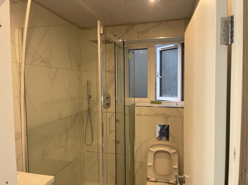 Finished shower room with large-format marble-effect wall tiles, a glass shower screen, a wall-hung toilet and a window