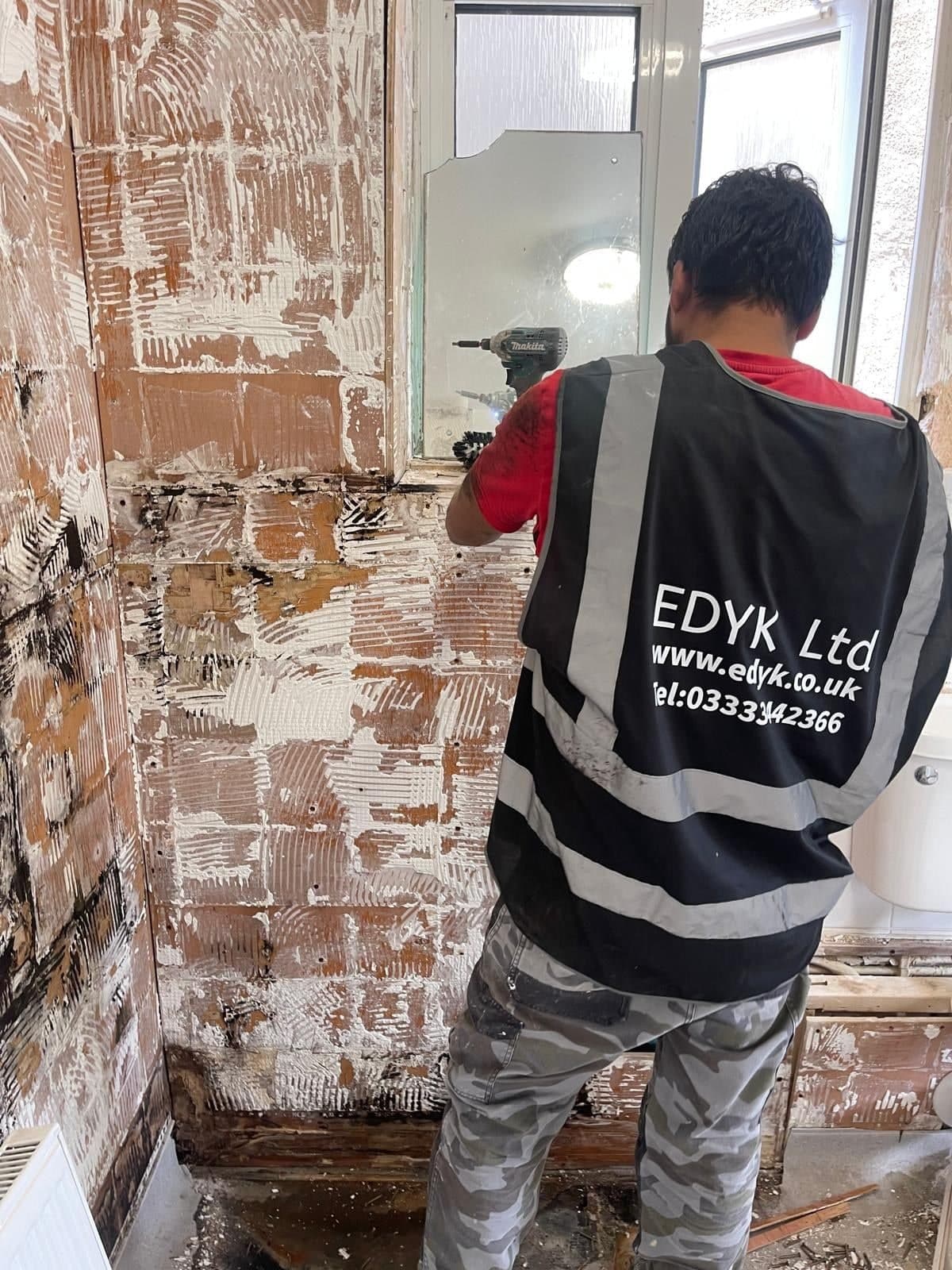 EDYK team member stripping out a bathroom in a flat, with the old wall tiles removed