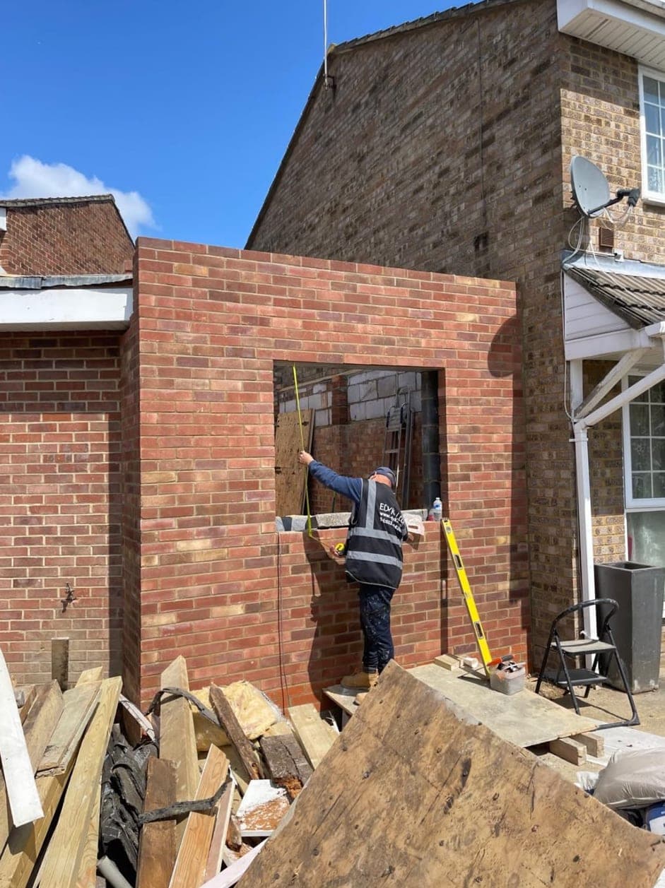 Team member measuring the window opening in new brickwork for the house extension, with timber off-cuts in the foreground