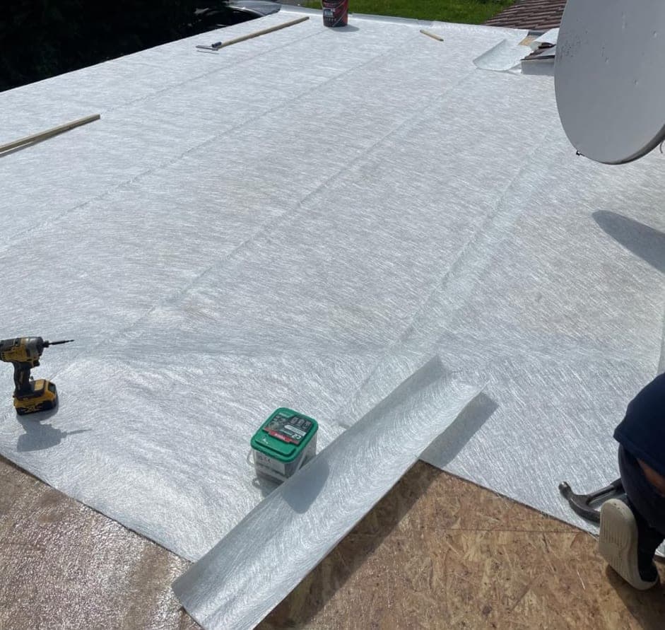 New flat roof of the house extension covered in grey membrane, with a drill and a tub of fixings on the roof