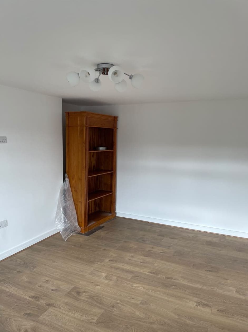 Finished room with white walls, laminate flooring and a wooden bookcase after the renovation