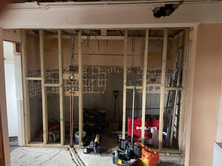 Timber stud wall framed up in a room during the renovation, with tools and materials on the floor and wiring above