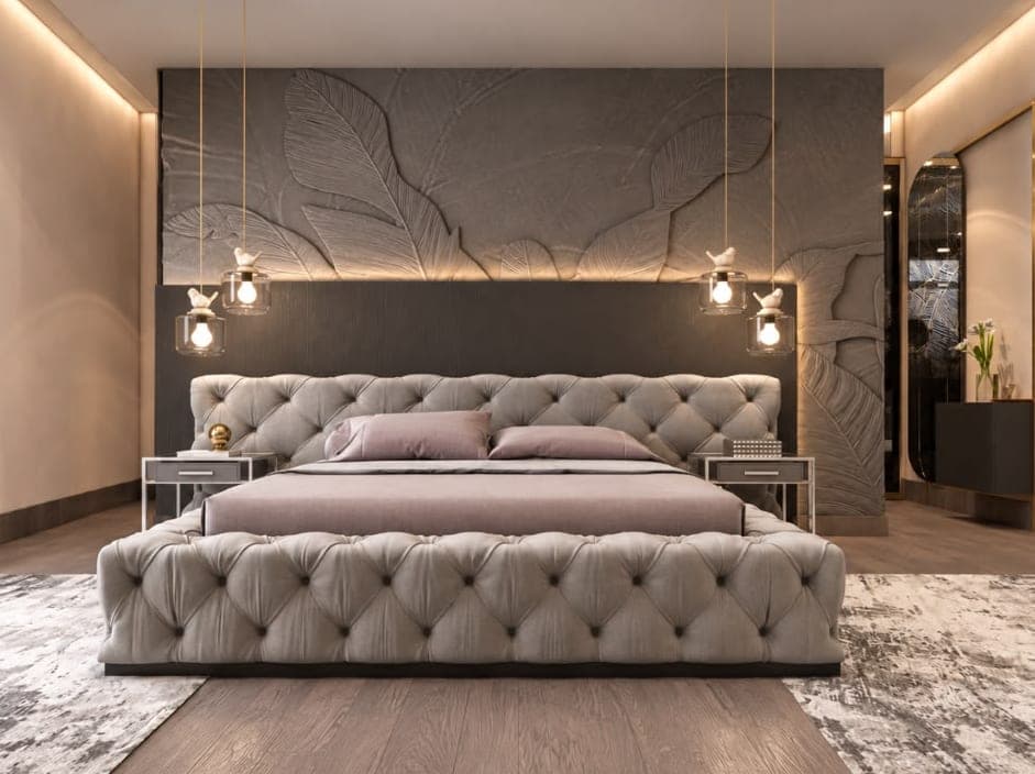 Apartment bedroom with a grey tufted bed, pendant lights and a carved feature wall behind the headboard