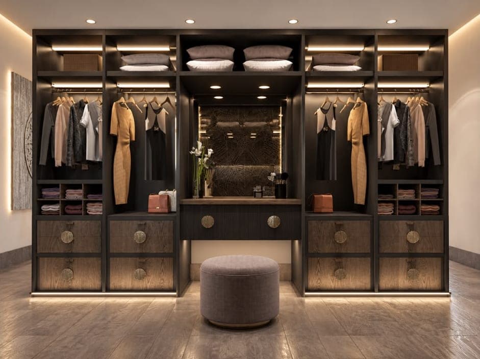 Apartment walk-in wardrobe with dark shelving, hanging rails, a central dressing table with a mirror and a round pouffe